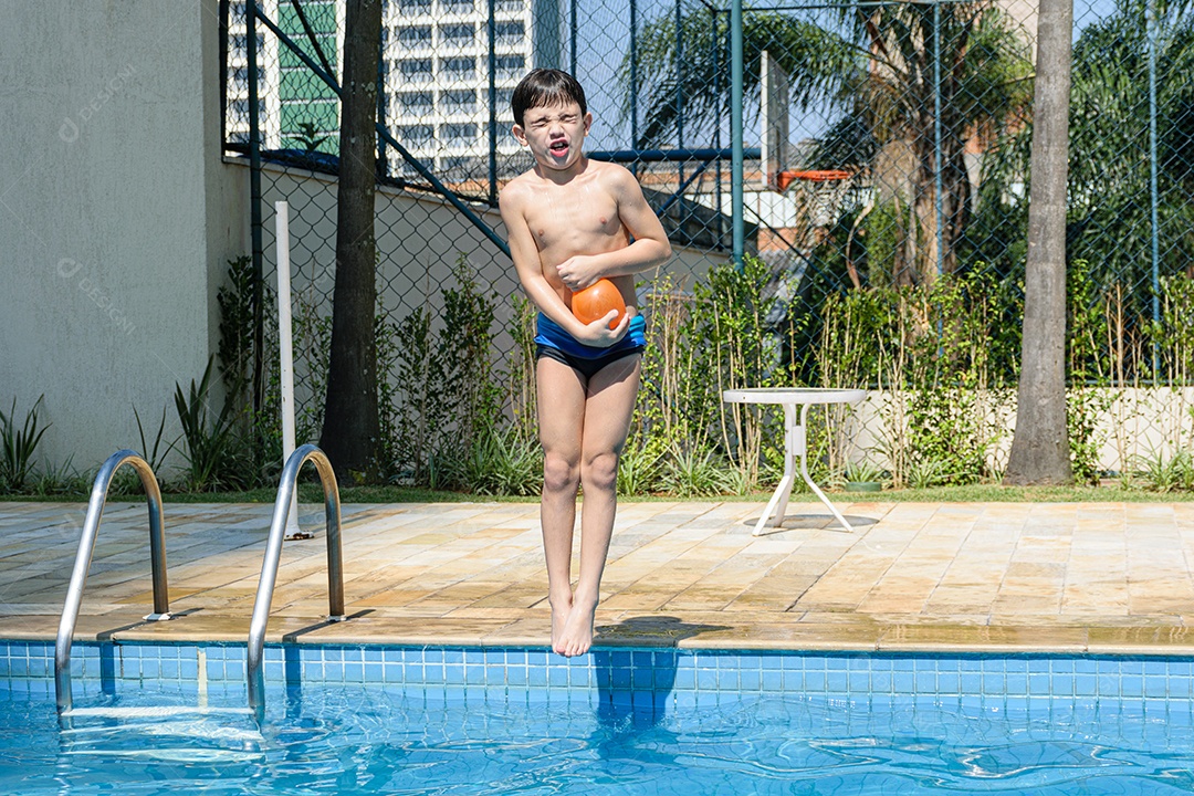 Criança de 8 anos fazendo careta e pulando na piscina com uma bomba dágua.