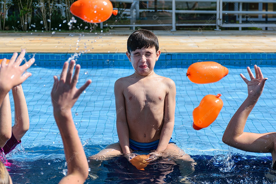 Criança de 8 anos sentada na beira da piscina, brincando com várias bombas dágua.