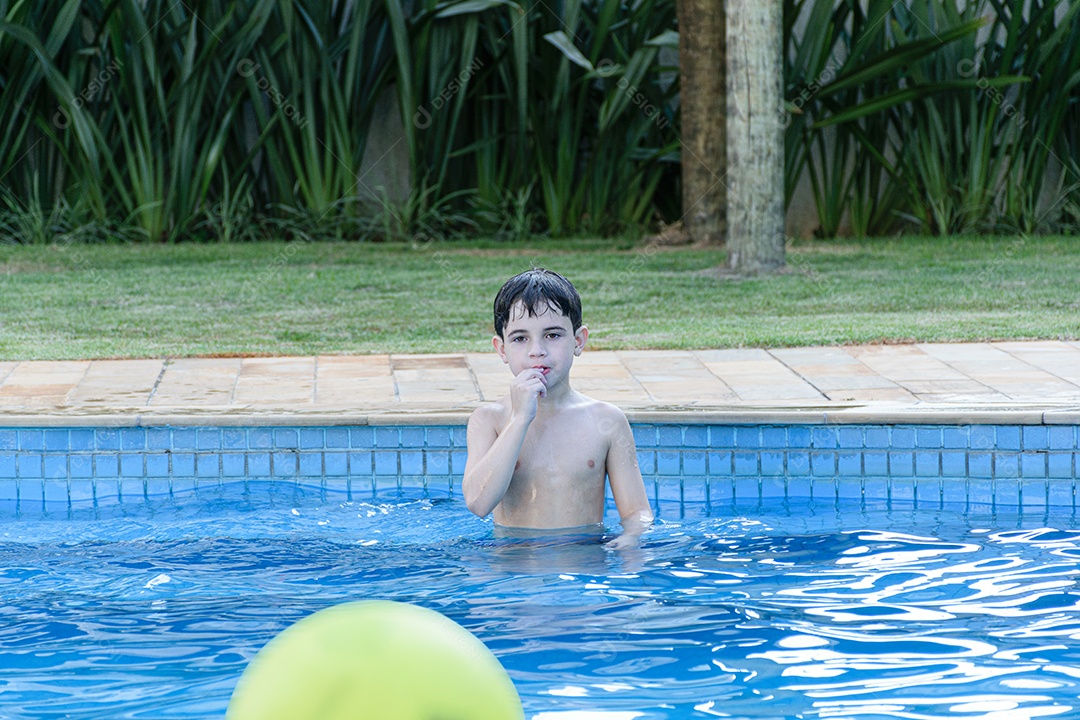 Criança de 8 anos na piscina, esperando a bola ser lançada para ele pegar.