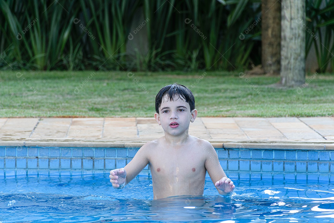 Criança de 8 anos na piscina, esperando a bola ser lançada para ele pegar.