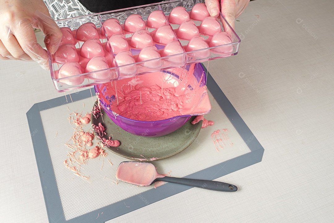 Confeiteiro despejando uma forma de policarbonato com ganache de morango em uma cápsula