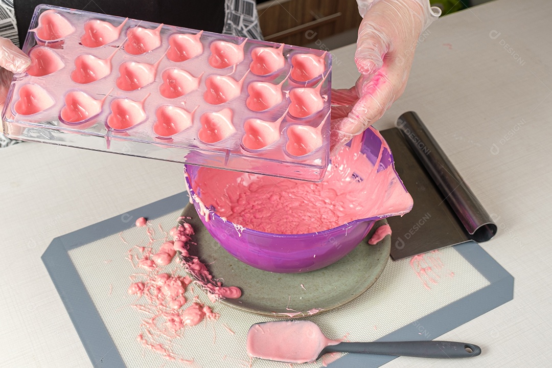 Confeiteiro segurando uma espátula e mostrando uma forma de policarbonato com ganache de morango