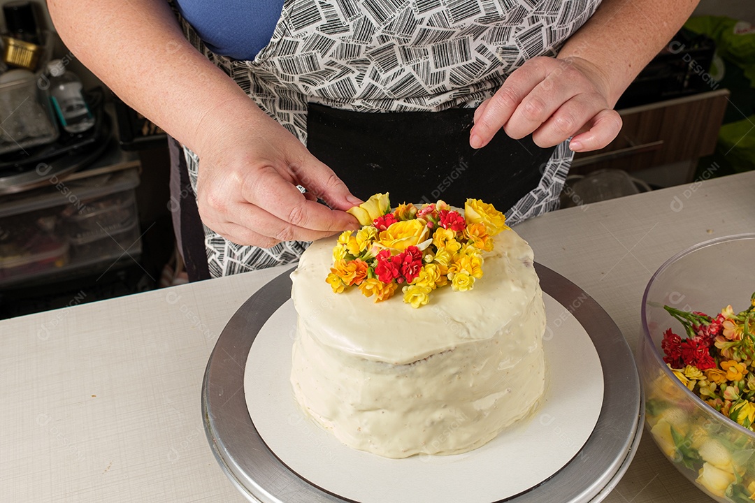 Bolo de baunilha sendo decorado com flores amarelas pelo chef confeiteiro