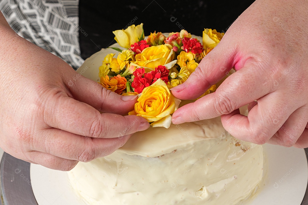Bolo de baunilha sendo decorado com flores amarelas pelo chef confeiteiro
