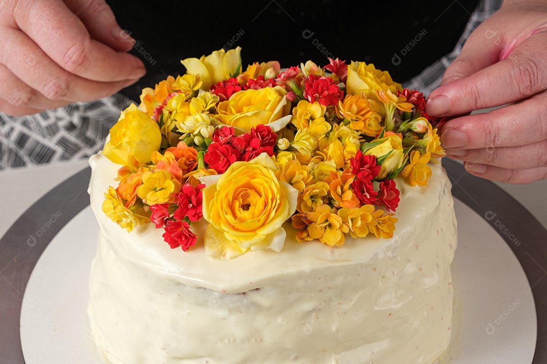 Bolo de baunilha sendo decorado com flores amarelas pelo chef confeiteiro