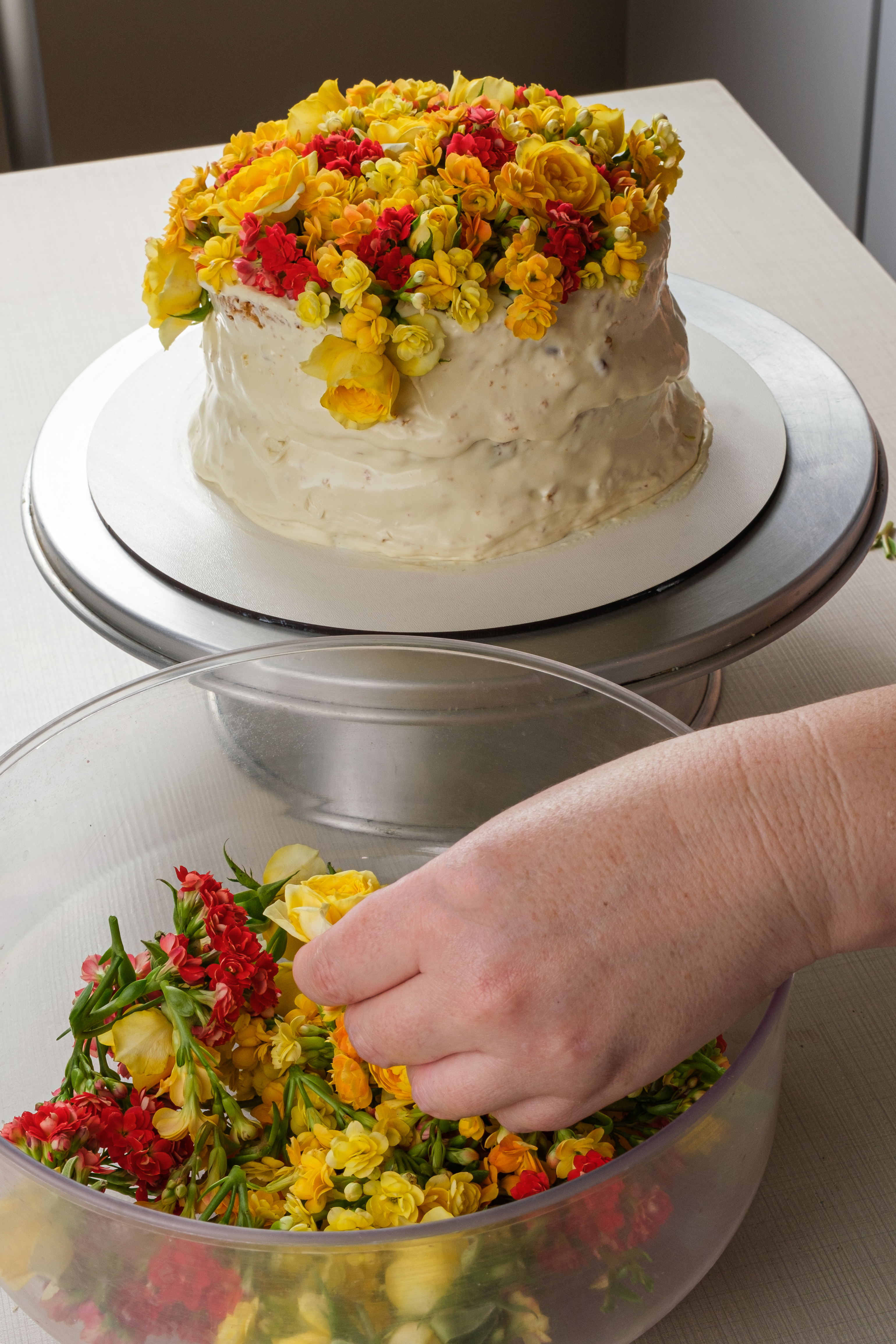 Bolo de baunilha sendo decorado com flores amarelas pelo chef confeiteiro