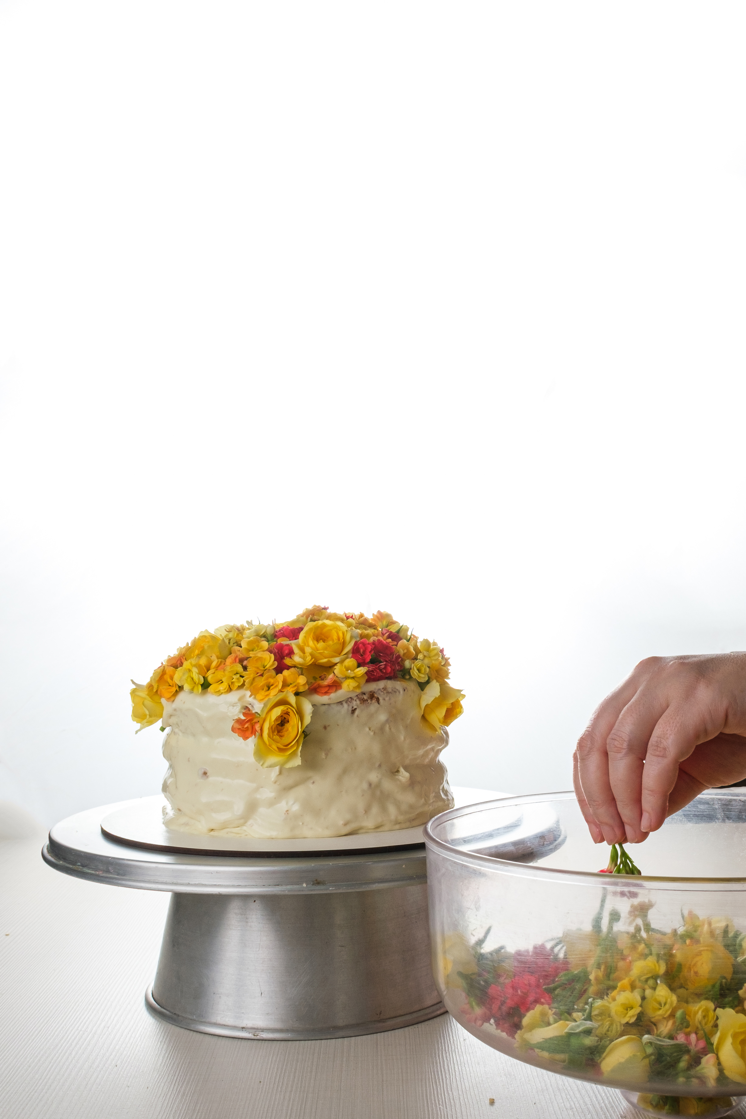 Bolo de baunilha sendo decorado com flores amarelas pelo chef confeiteiro