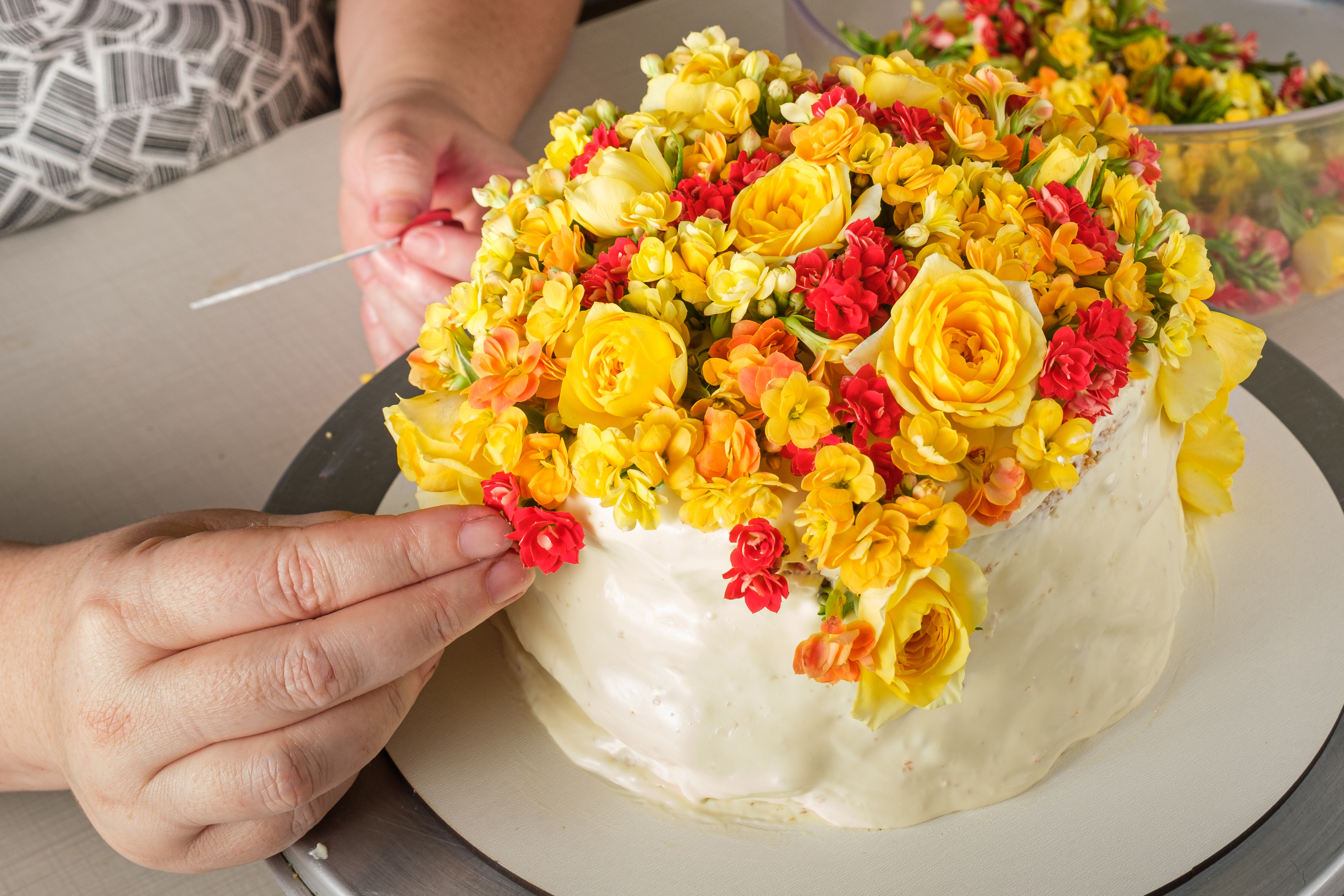 Bolo de baunilha sendo decorado com flores amarelas pelo chef confeiteiro