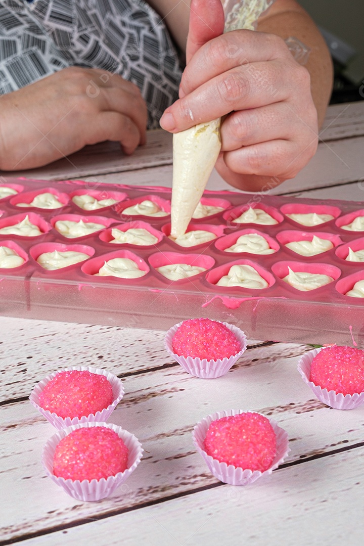 Bicho de pe, doce brasileiro. Ao fundo, uma confeiteira recheando bombons com ganache