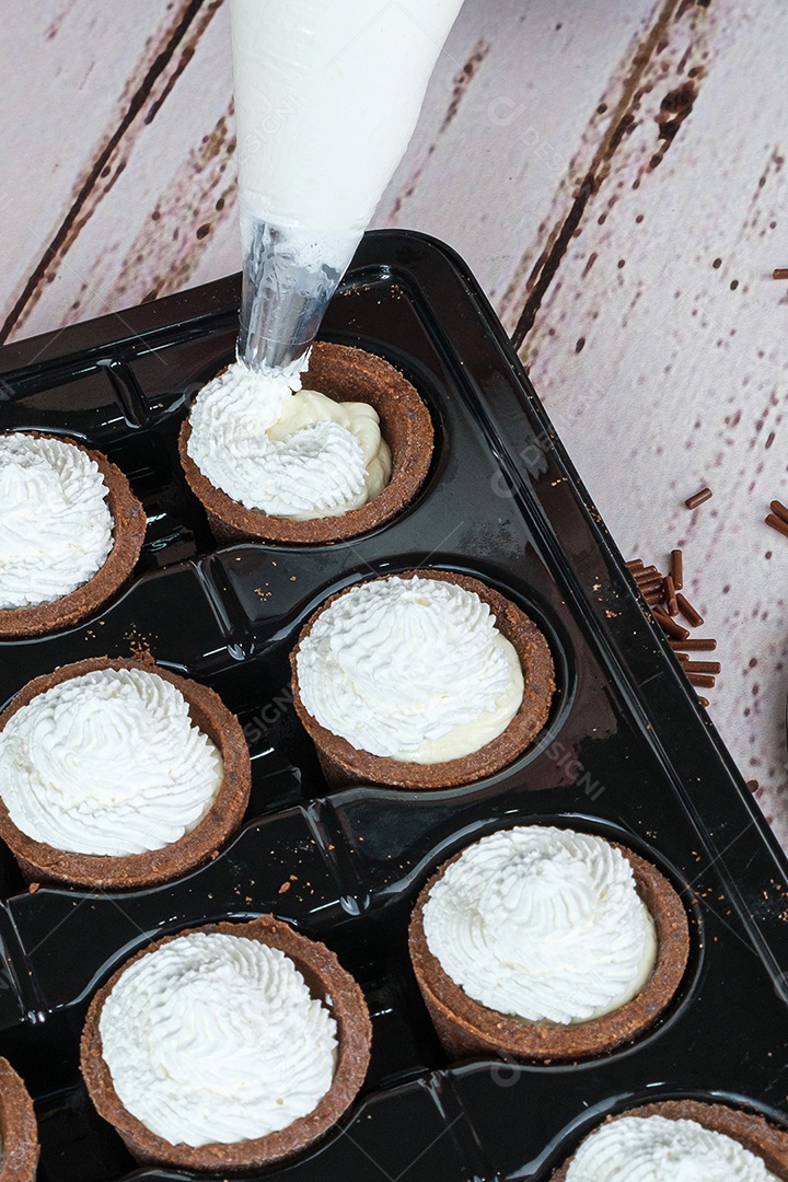 Detalhe do bocal de confeiteiro recheando mini ganache de chocolate branco com tortinhas de chocolate
