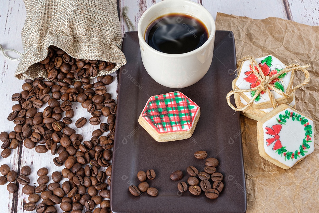 Biscoitos amanteigados com tema natalino ao lado de grãos de café e xícara.