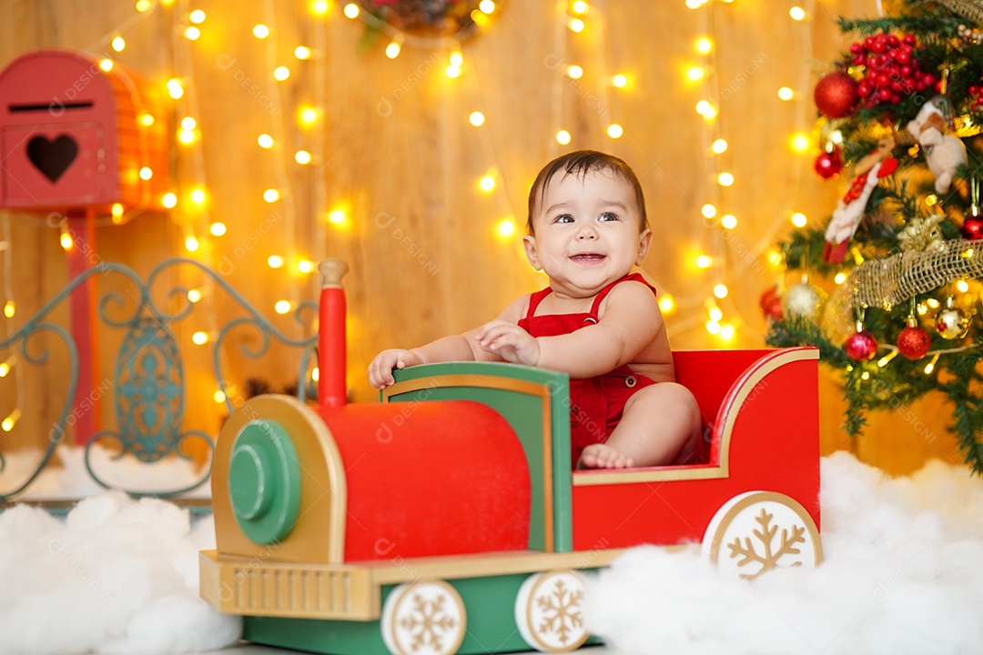 Linda criança sentada em trenzinho sobre cénario natalino