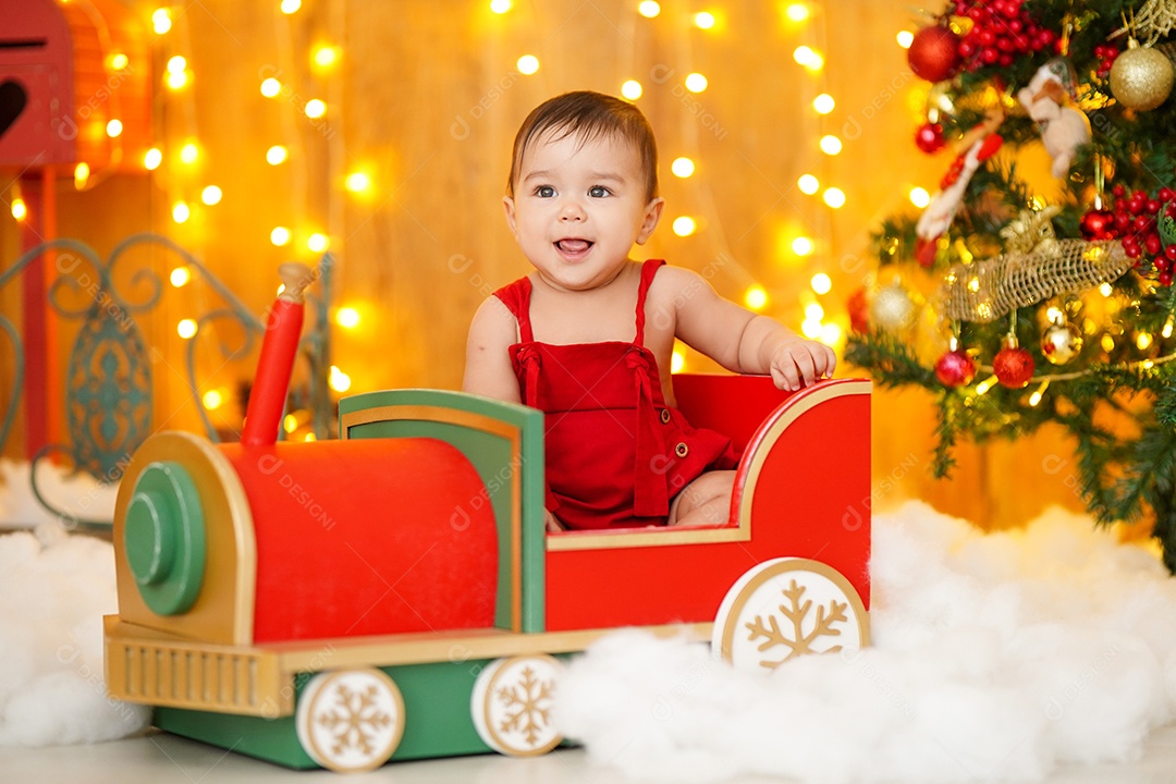 Linda criança sentada em trenzinho sobre cénario natalino