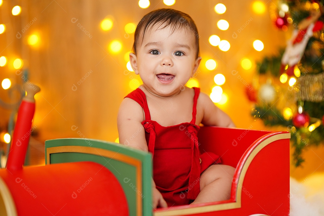 Linda criança sentada em trenzinho sobre cénario natalino