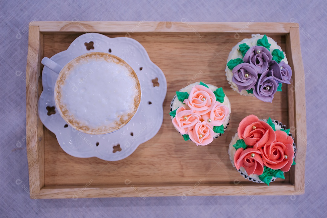 Bandeja de madeira com cupcakes decorados e xícara de cappuccino