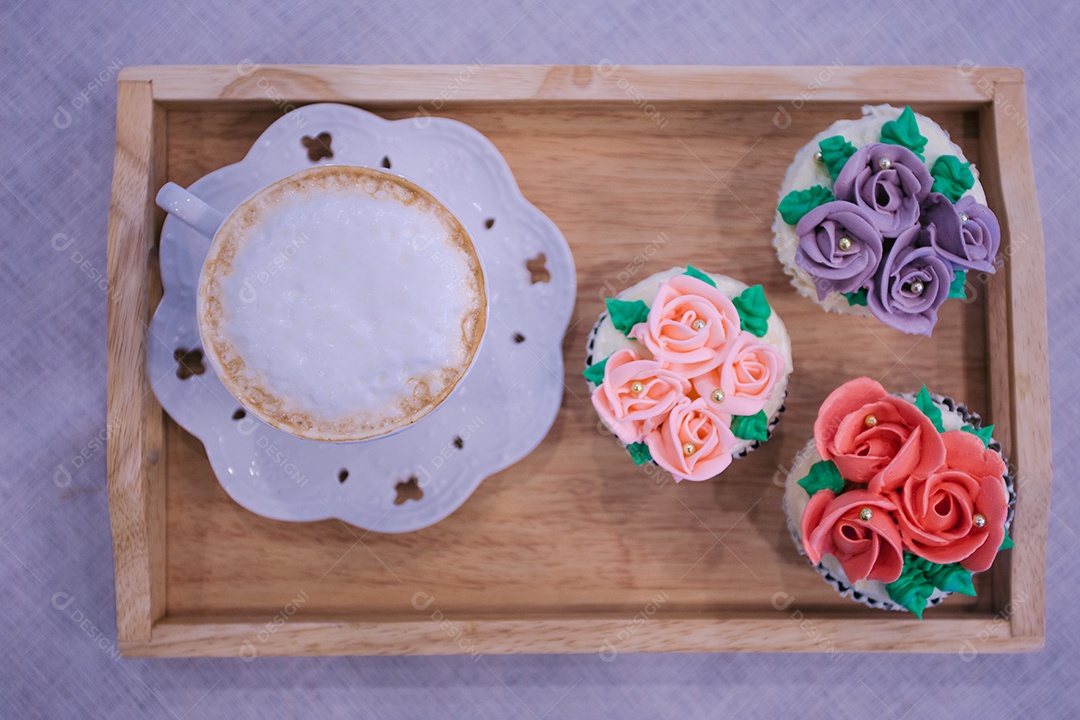 Bandeja de madeira com cupcakes decorados e xícara de cappuccino