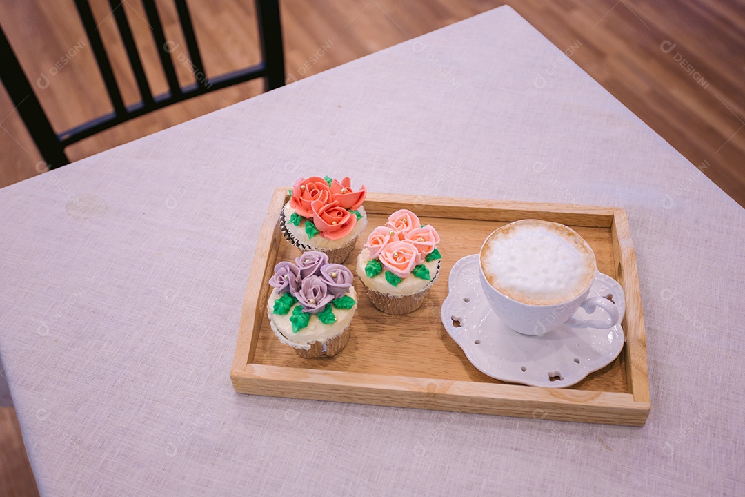 Bandeja de madeira com cupcakes decorados e xícara de cappuccino