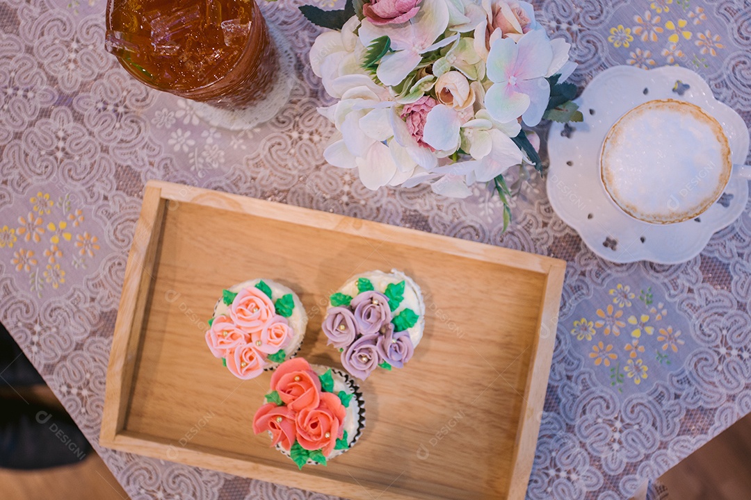 Bandeja de madeira com cupcakes decorados e xícara de cappuccino