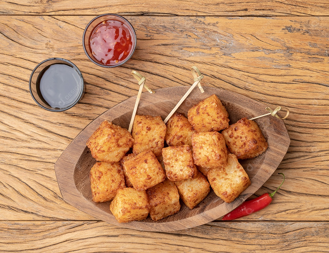 Dado de tapioca, comida típica do nordeste brasileiro com calda de pimenta malagueta sobre mesa de madeira.