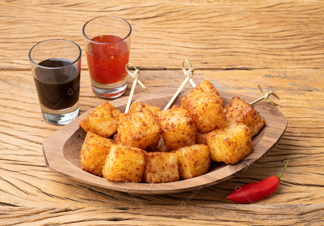 Dado de tapioca, comida típica do nordeste brasileiro com calda de pimenta malagueta sobre mesa de madeira.