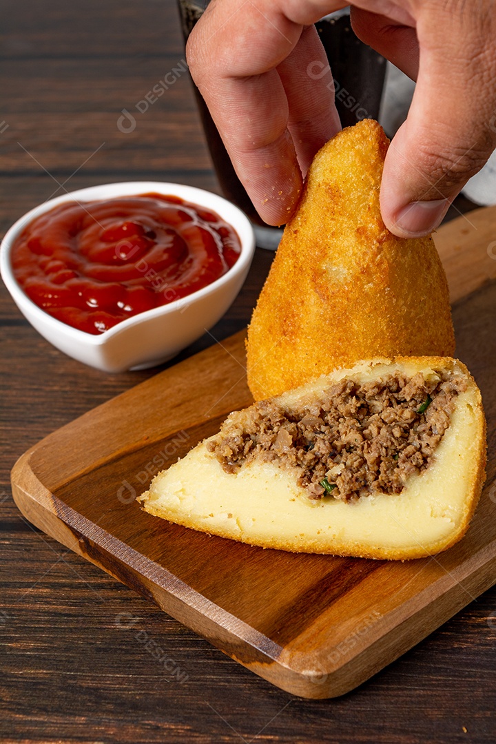 Coxinha lanche tradicional brasileiro frito em óleo e recheado com carne bovina ou carne de frango, com ketchup e refrigerante no fundo sobre mesa de madeira. foto vertical