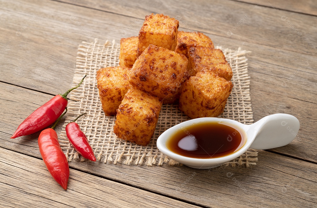 Dado de tapioca, comida típica do nordeste brasileiro com calda de pimenta malagueta sobre mesa de madeira.