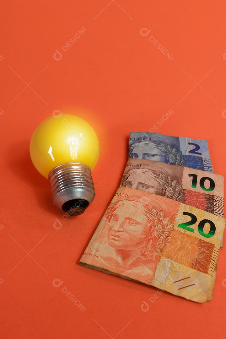 Dinheiro brasileiro e lâmpada isolados em fundo laranja. Imagem de crises de energia leve.
