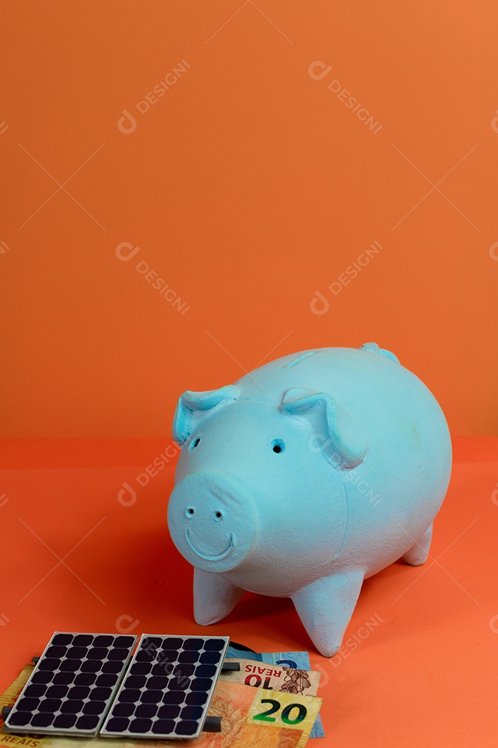 Cofrinho, painel de energia solar fotovoltaica e dinheiro brasileiro isolado em fundo laranja.