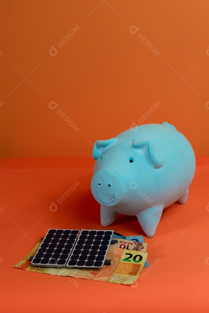 Cofrinho, painel de energia solar fotovoltaica e dinheiro brasileiro isolado em fundo laranja.
