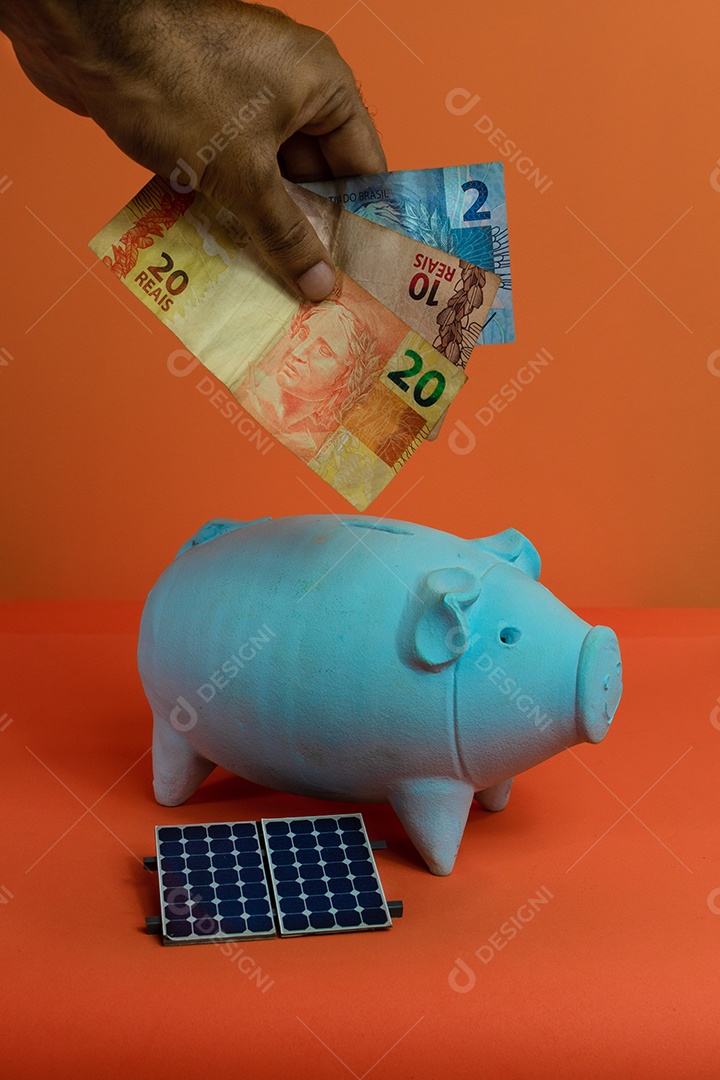 Colocando dinheiro brasileiro real no cofrinho isolado em fundo laranja.