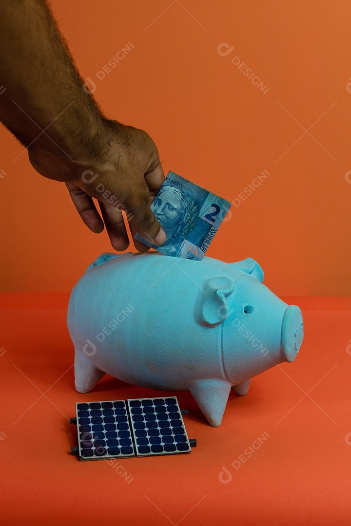 Colocando dinheiro brasileiro real no cofrinho isolado em fundo laranja.