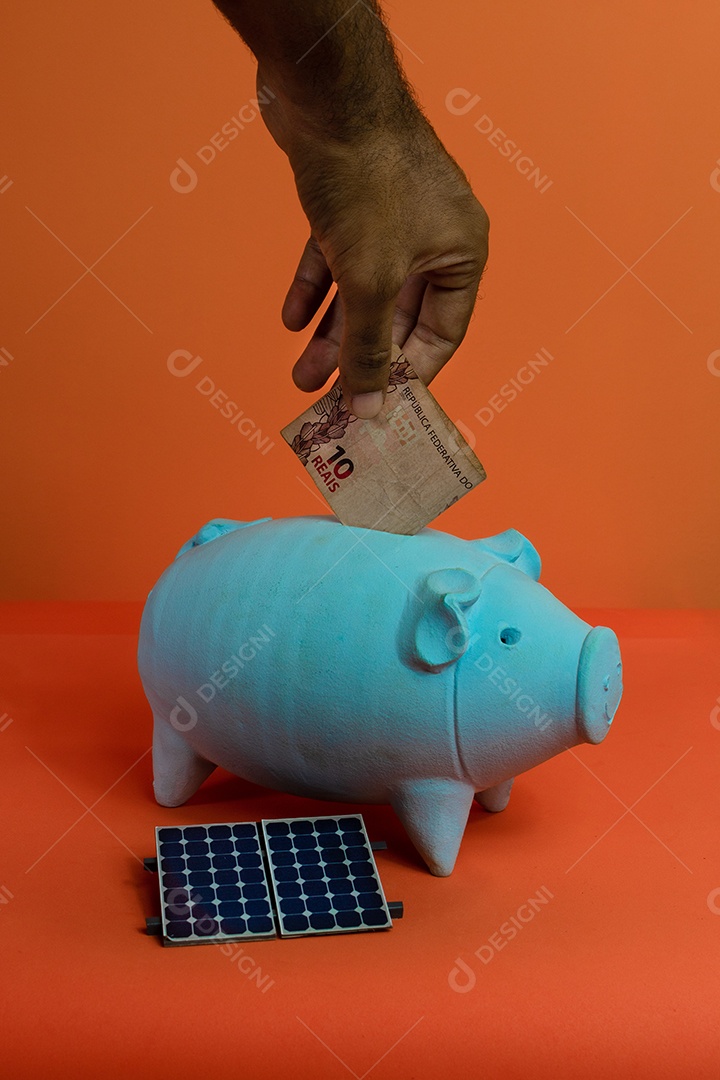 Colocando dinheiro brasileiro real no cofrinho isolado em fundo laranja.