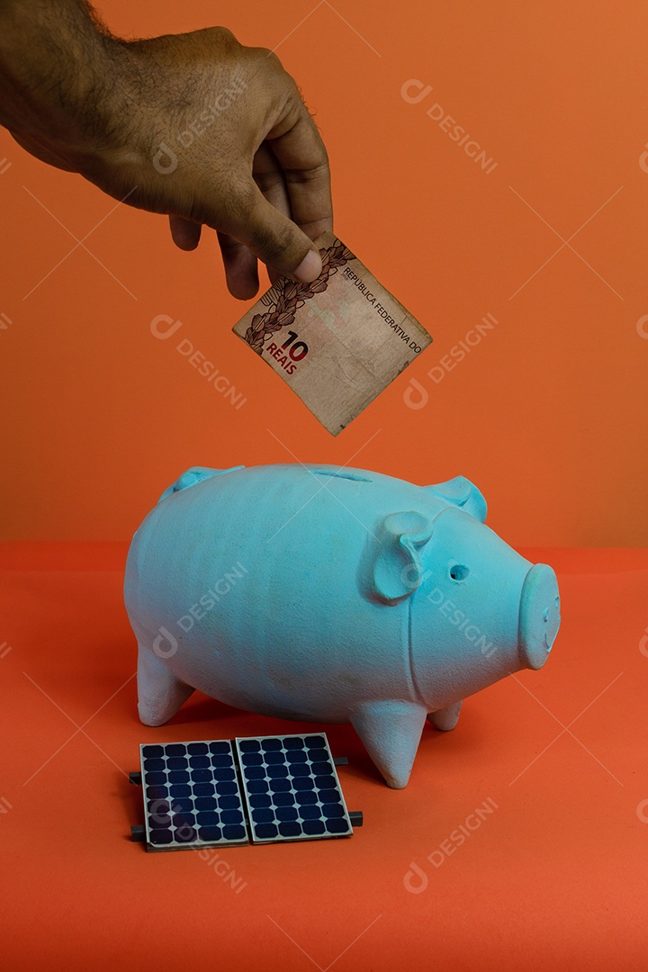 Colocando dinheiro brasileiro real no cofrinho isolado em fundo laranja.