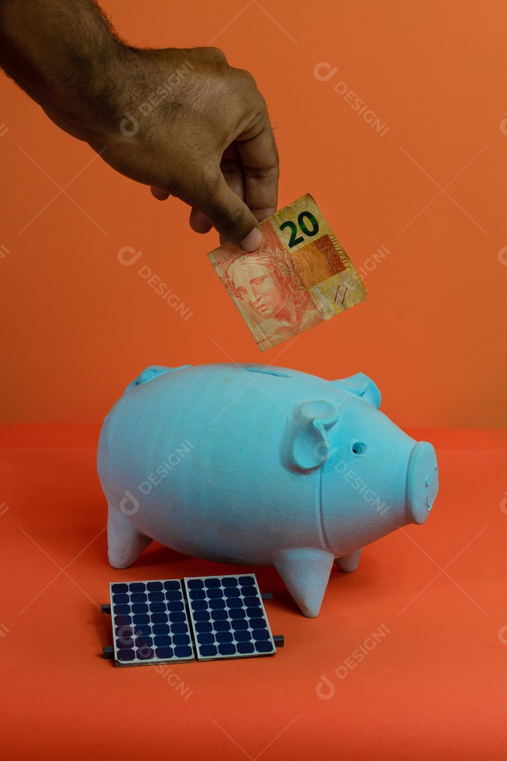 Colocando dinheiro brasileiro real no cofrinho isolado em fundo laranja.