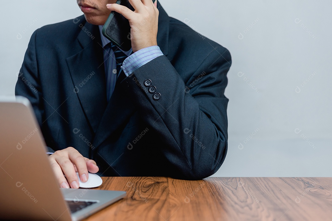 Empresário trabalhando no laptop e falando ao telefone do escritório moderno.