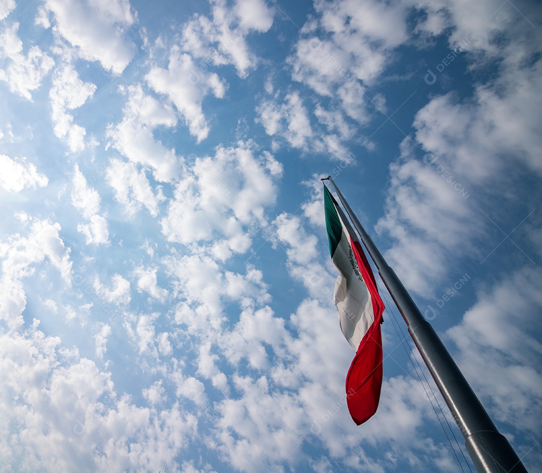 Bandeira mexicana tremulando sobre um céu nublado.