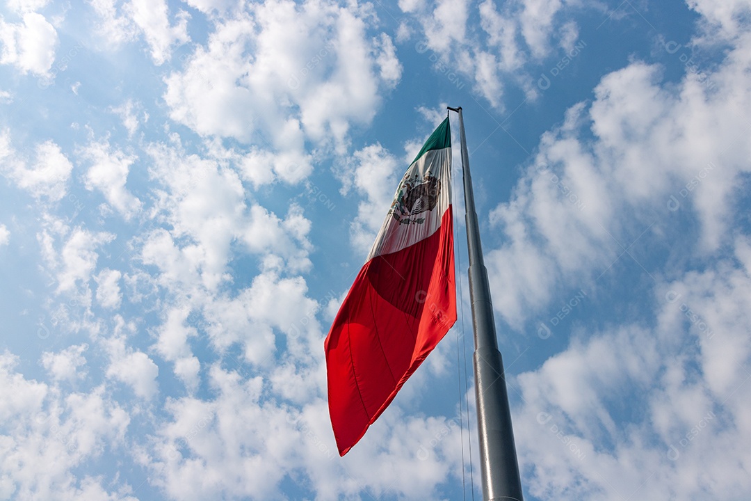 Bandeira mexicana tremulando sobre um céu nublado.