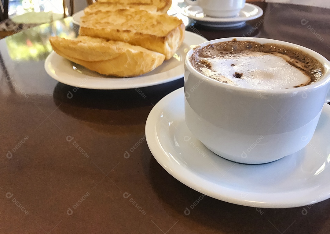 Pão torrado com manteiga na chapa e capuccino na mesa de madeira. Café da Manhã