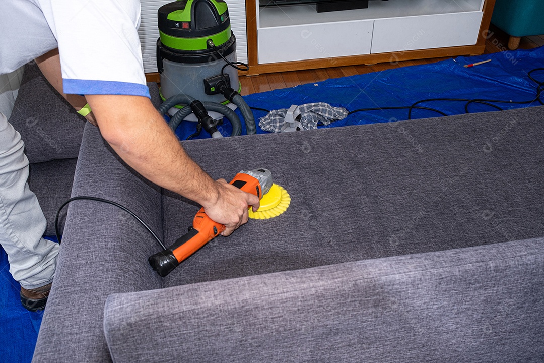 Homem com escova polidora elétrica limpando um sofá cinza