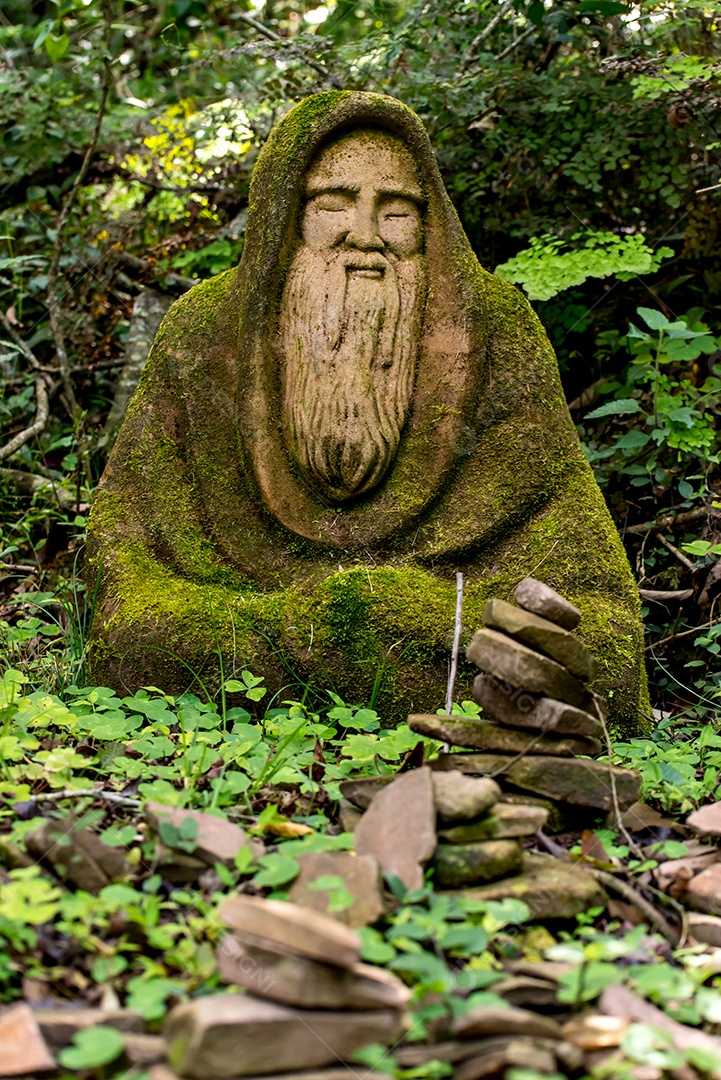 Estátua de um homem barbudo meditando no meio da floresta,
