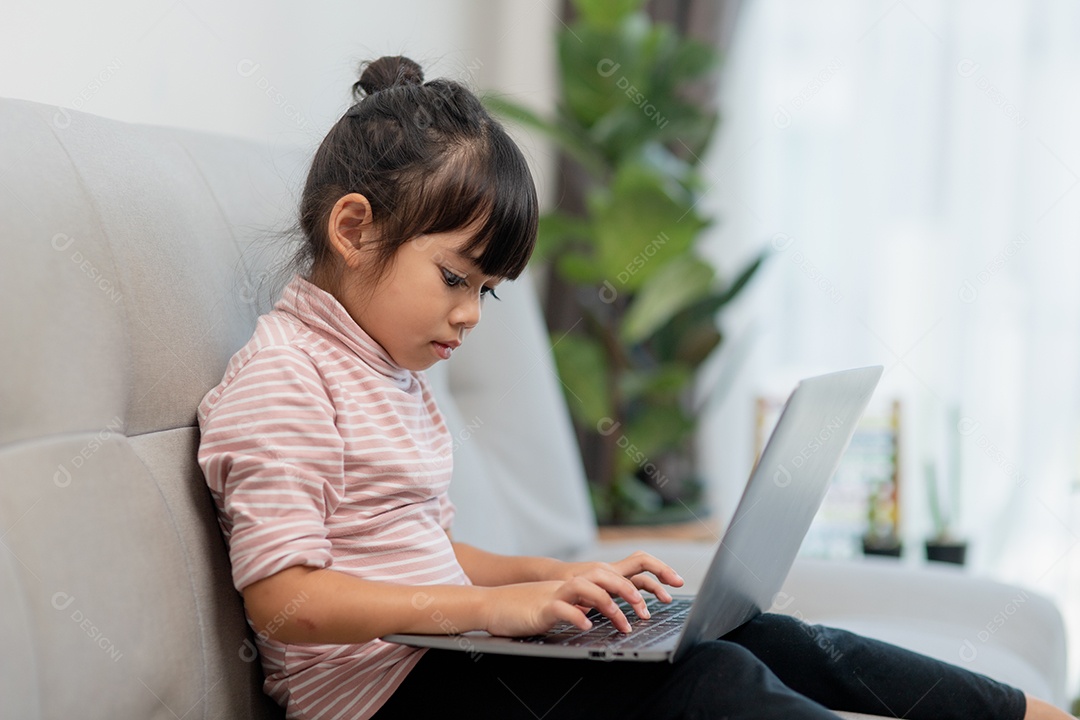 Garotinha asiática usa laptop sentado no sofá