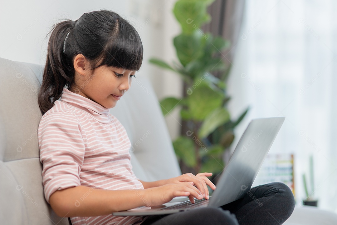 Garotinha asiática usa laptop sentado no sofá