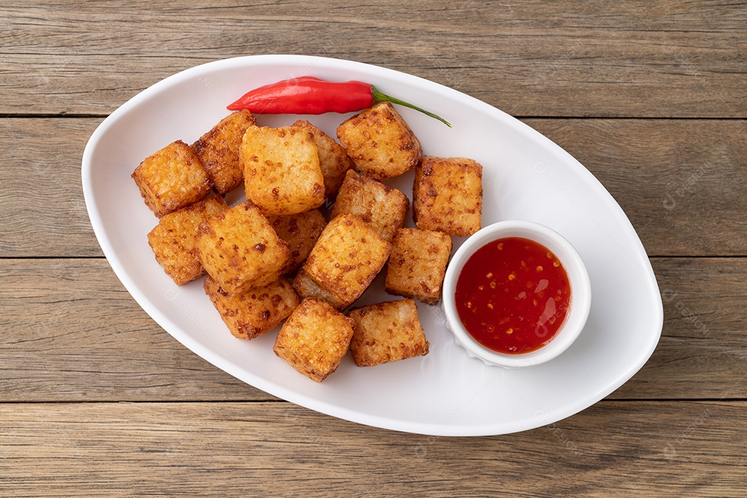 Dado de tapioca, comida com calda de pimenta malagueta sobre mesa de madeira.