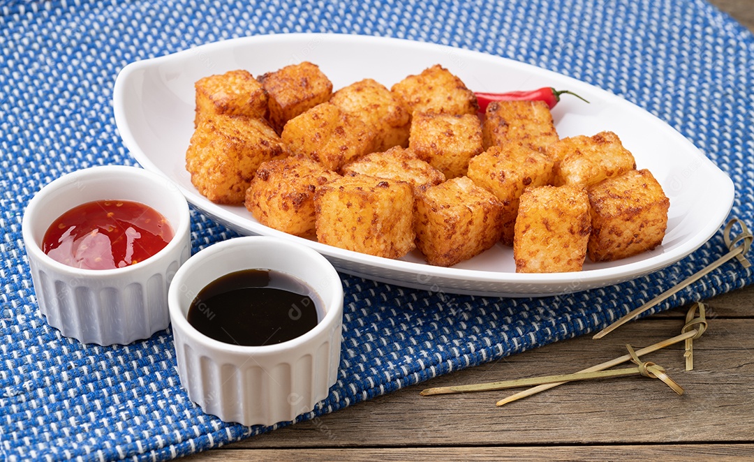 Dado de tapioca, comida com calda de pimenta malagueta sobre mesa de madeira.