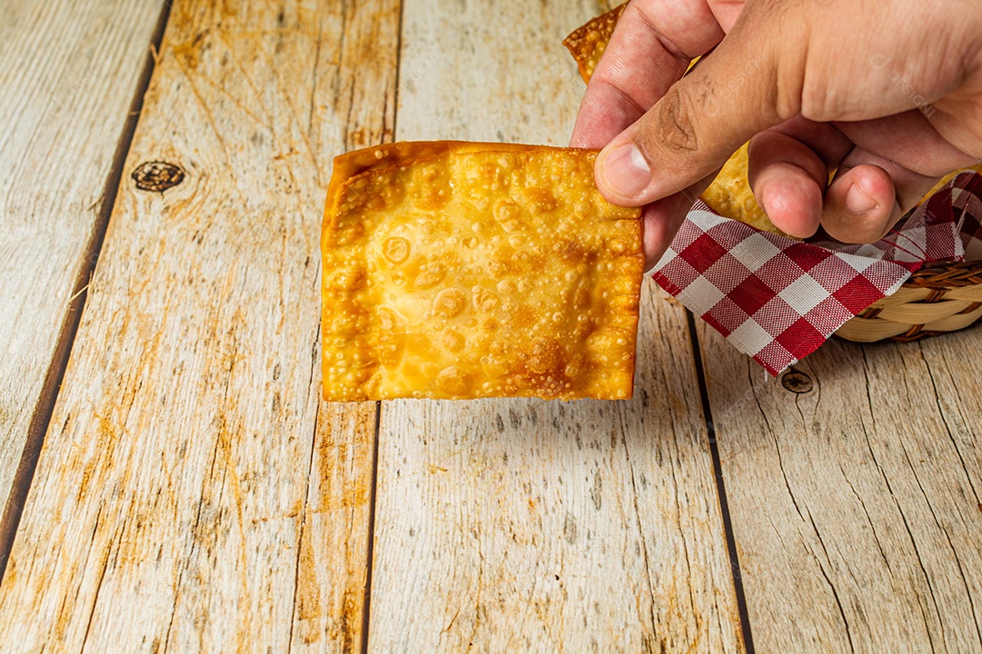 Mão masculina segurando um lanche brasileiro pastel frito frito em óleo quente