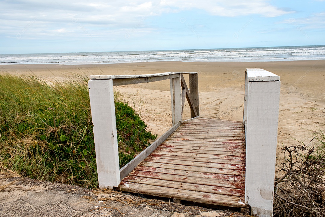 Caminho de madeira para a areia da praia com o mar ao fundo