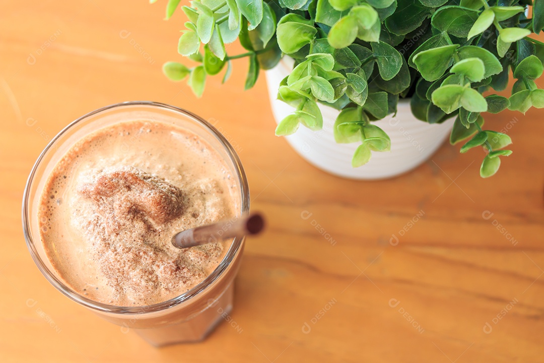 Milkshake de cacau sobre mesa de madeira com planta artificial