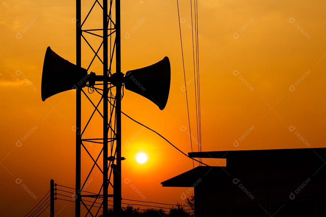 Alto falante em pilar de metal acima do telhado de uma casa no crepúsculo na Tailândia