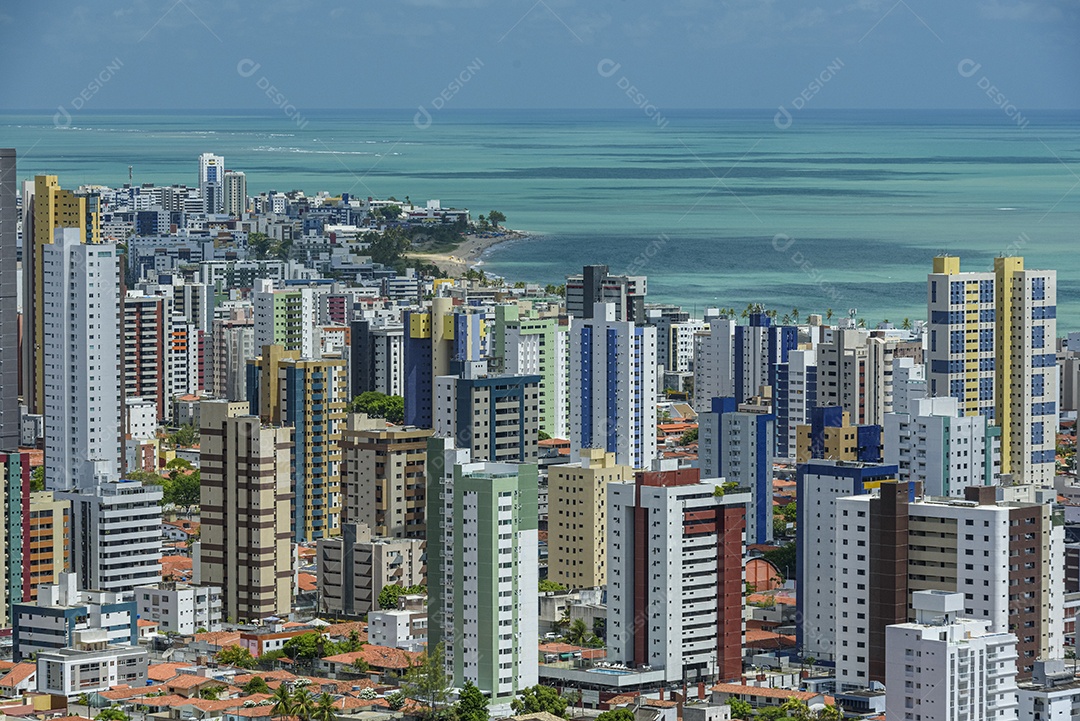 Vista parcial da cidade mostrando casas, prédios e a praia do Bessa ao fundo.