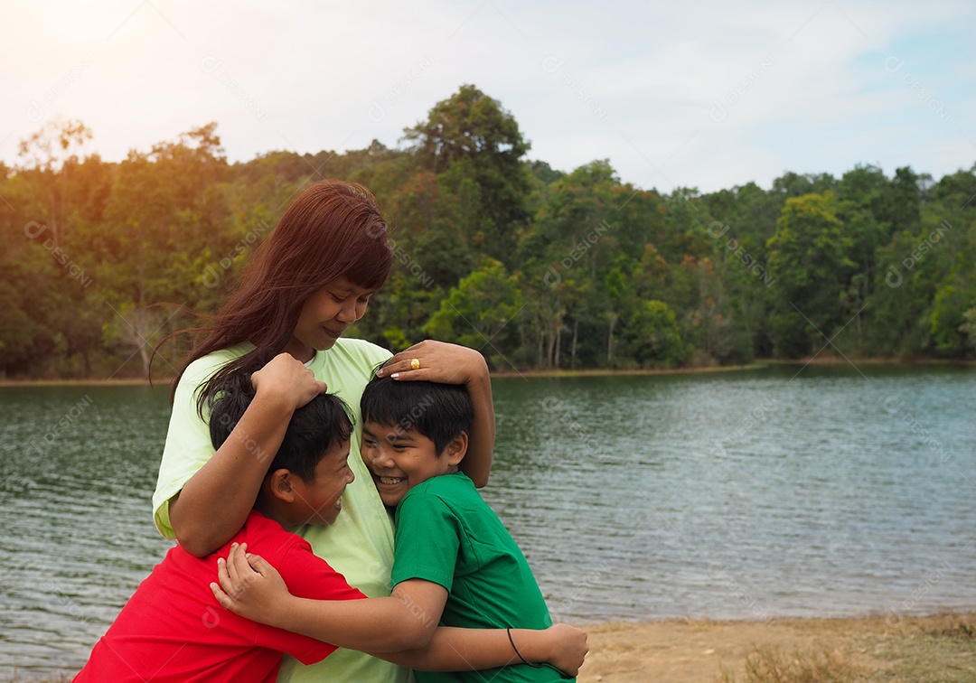Família feliz passando tempo ao ar livre abraçando e apreciando a vista do rio. Mãe com dois filhos.